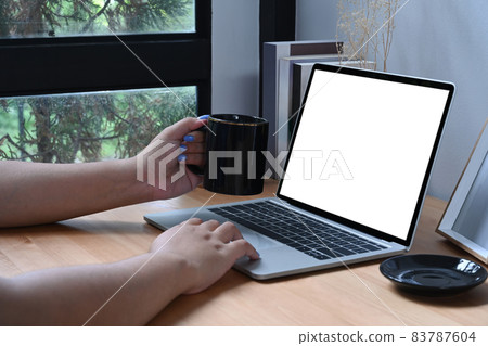 Young woman holding cup of coffee and using computer laptop at home. Young woman holding cup of coffee and using computer laptop at home. 83787604