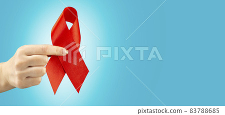 Health care and medicine concept. AIDS awareness. A female hand holds a red AIDS awareness ribbon on a blue background with place for text. International AIDS Day 83788685