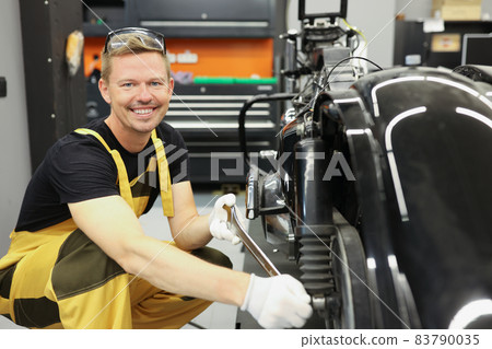 Smiling mechanic spinning motorcycle wheel with wrench in work shop Smiling mechanic spinning motorcycle wheel with wrench in work shop 83790035