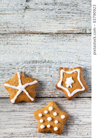 Border of Christmas gingerbreads in the shape of a star with patterns of glaze and spices on a white wooden background. 83790923