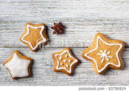 Border of Christmas gingerbreads in the shape of a star with patterns of glaze and spices on a white wooden background. Border of Christmas gingerbreads in the shape of a star with patterns of glaze and spices on a white wooden background. 83790924
