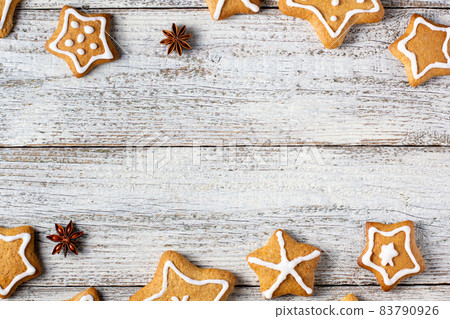 Border of Christmas gingerbreads in the shape of a star with patterns of glaze and spices on a white wooden background. Border of Christmas gingerbreads in the shape of a star with patterns of glaze and spices on a white wooden background. 83790926