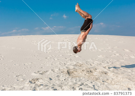 Portrait of young parkour man doing flip or somersault on the sand. Portrait of young parkour man doing flip or somersault on the sand. 83791373