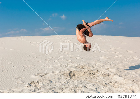 Portrait of young parkour man doing flip or somersault on the sand. Portrait of young parkour man doing flip or somersault on the sand. 83791374