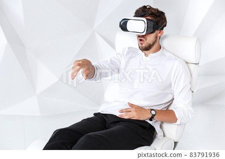 Excited young man is getting experience using VR-headset glasses of virtual reality gesticulating with his hands Excited young man is getting experience using VR-headset glasses of virtual reality gesticulating with his hands 83791936