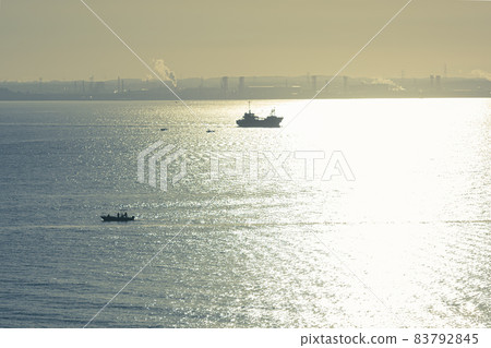 Tokyo Bay illuminated by the early morning sun, the sea reflected by the backlit morning sun, a ship passing through an industrial area Tokyo Bay illuminated by the early morning sun, the sea reflected by the backlit morning sun, a ship passing through an industrial area 83792845