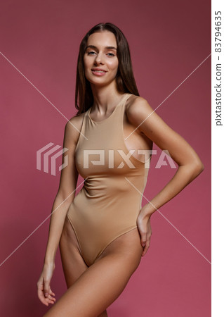 Portrait of young beautiful slim girl in nude color lingerie posing isolated over dark pink studio background. Natural beauty concept. Portrait of young beautiful slim girl in nude color lingerie posing isolated over dark pink studio background. Natural beauty concept. 83794635