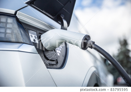 Charging connector connected to the electrical socket of a hybrid car. 83795595