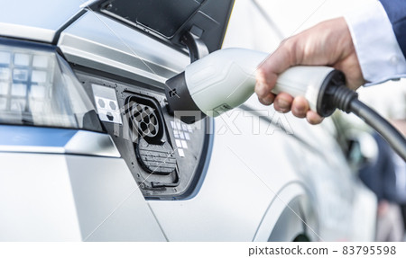 The driver of the electric car inserts the electrical connector to charge the batteries. 83795598