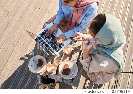 Islamic sisters in hijab making calls and working with gadgets during the coffee break 83796919