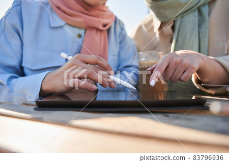 Two women in scarfs involved at the working with tablet 83796936