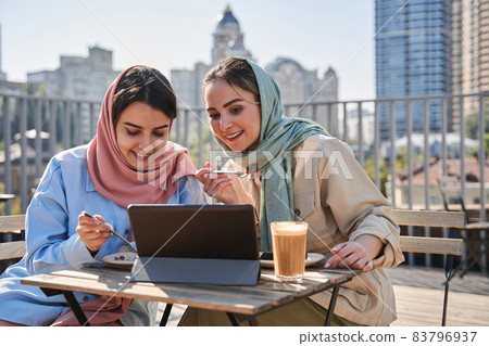 Hijab girls watching something at the tablet during the dinner at the cafe Hijab girls watching something at the tablet during the dinner at the cafe 83796937