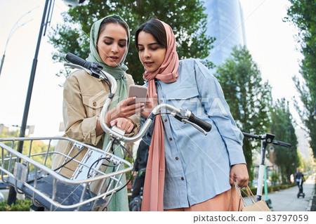 Millennial muslim woman in abayas using smartphone to unlocking urban bike 83797059