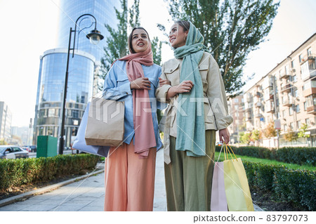 Two female muslim shopaholics walking through the street after great shopping Two female muslim shopaholics walking through the street after great shopping 83797073