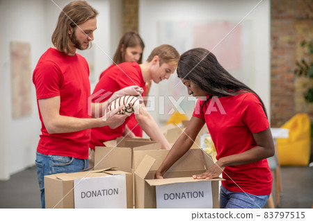Young volunteers in red tshirts distributing donations in a sorting center Young volunteers in red tshirts distributing donations in a sorting center 83797515