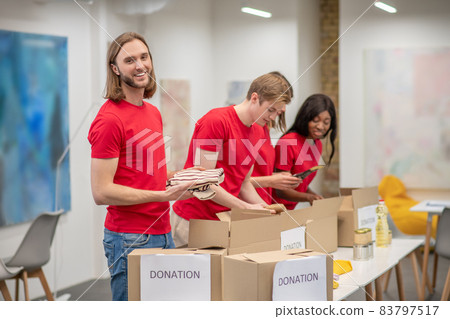 Young peeple in red packing the cardboards with humanitarian help 83797517