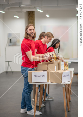Young peeple in red packing the cardboards with humanitarian help 83797521