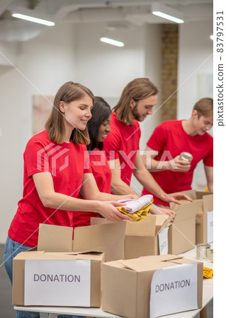 Young peeple in red packing the cardboards with humanitarian help Young peeple in red packing the cardboards with humanitarian help 83797531