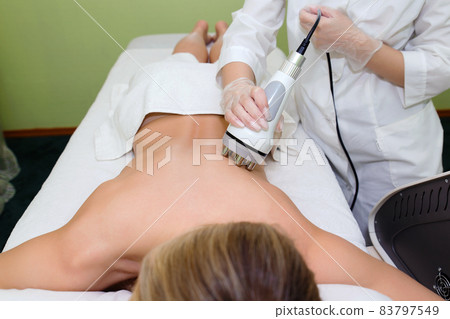 A young woman is carried out radiofrequency lifting to get rid of fat in the lateral places of the body. The cosmetologist conducts hardware cosmetology in the beauty salon. A young woman is carried out radiofrequency lifting to get rid of fat in the lateral places of the body. The cosmetologist conducts hardware cosmetology in the beauty salon. 83797549