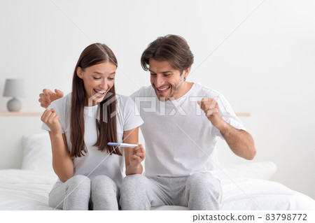 Glad excited millennial european man and woman rejoicing positive pregnancy test on bed in bedroom 83798772