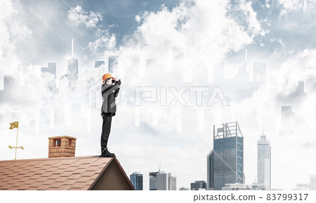 Engineer man standing on roof and looking in binoculars. Mixed m 83799317