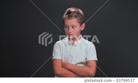 Caucasian 10 years boy looks side ways in surprise or terrified. Child with his arms folded poses on black background. Surprise or scare concept Caucasian 10 years boy looks side ways in surprise or terrified. Child with his arms folded poses on black background. Surprise or scare concept 83799517