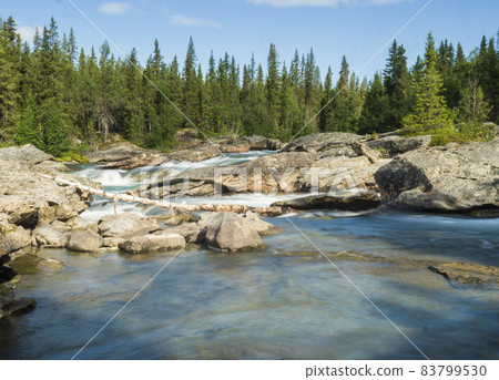Beautiful landscape with long exposure water stream and cascade of river Kamajokk, boulders and spruce tree forest in Kvikkjokk village in Swedish Lapland. Summer sunny day, blue sky, white clouds Beautiful landscape with long exposure water stream and cascade of river Kamajokk, boulders and spruce tree forest in Kvikkjokk village in Swedish Lapland. Summer sunny day, blue sky, white clouds 83799530