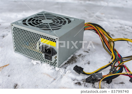 A computer power supply lies in a landfill in the snow 83799740