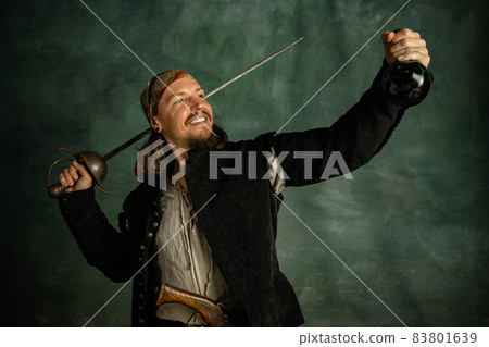 Portrait of one smiling man, medeival pirate holding bottle of rum isolated over dark background. Portrait of one smiling man, medeival pirate holding bottle of rum isolated over dark background. 83801639