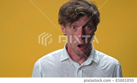 Young man making funny silly facial emotions isolated on yellow background. Weird dorky face of a handsome young man in white shirt. High quality 4k resolution footage 83801850