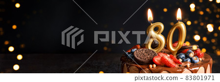 Banner with Chocolate birthday cake with berries, cookies and number eighty golden candles on black background, copy space 83801971