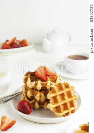 Delicious breakfast. Belgian waffles with honey and strawberries. Cup of tea white wooden background, top view. 83802726