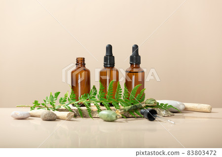 Amber glass transparent bottles on wooden podium with Jade face roller, leaves and natural stones Amber glass transparent bottles on wooden podium with Jade face roller, leaves and natural stones 83803472