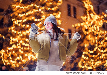 smiling adult girl takes selfie outdoors while standing in front of Christmas holidays decorations 83809577
