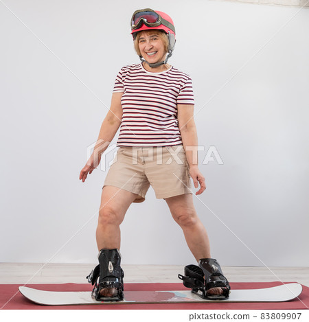 Elderly woman imitates snowboarding in the studio on a white background. 83809907