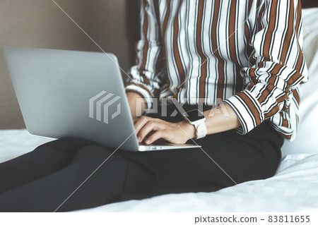 Woman sitting in bed indoors and using a laptop Woman sitting in bed indoors and using a laptop 83811655