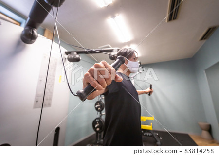 A man (mask) using a cable machine at a sports gym 83814258