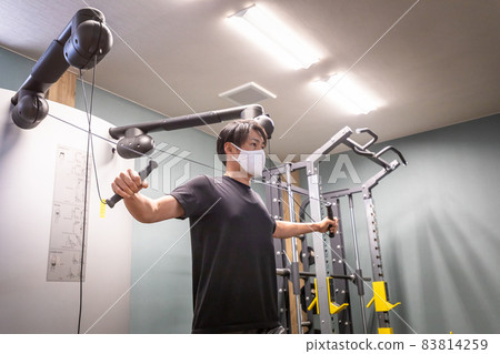A man (mask) using a cable machine at a sports gym 83814259