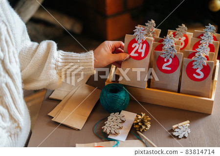Close-up top view of unrecognizable young woman sticks number on craft bag, fastens with clothespin and puts away in wooden tray. 83814714