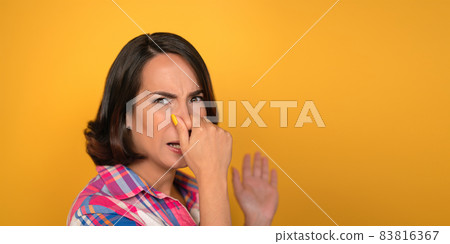 Young woman covered her nose with hand. Caucasian brunette expression that smells bad. Cut out on yellow background. Copy space at right Young woman covered her nose with hand. Caucasian brunette expression that smells bad. Cut out on yellow background. Copy space at right 83816367