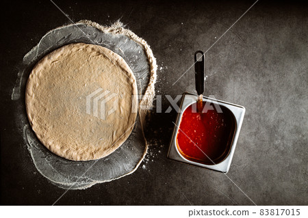 Making a pizza spreding tomato sauce on the dough 83817015