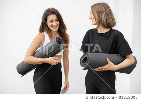 Girls stand with fitness mats and talk outdoors Girls stand with fitness mats and talk outdoors 83819005