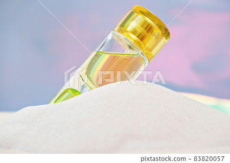 a bottle of bright yellow perfume on a sandy beach. light and airy summer fragrances for women. scents for holiday 83820057