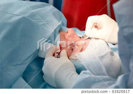 Close up of the face of a patient who is undergoing blepharoplasty. The surgeon cuts the eyelid and performs manipulations using medical instruments Close up of the face of a patient who is undergoing blepharoplasty. The surgeon cuts the eyelid and performs manipulations using medical instruments 83820817