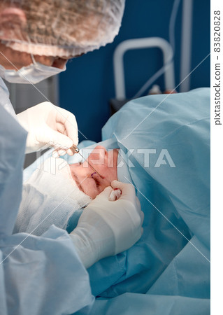 Close up of the face of a patient who is undergoing blepharoplasty. The surgeon cuts the eyelid and performs manipulations using medical instruments Close up of the face of a patient who is undergoing blepharoplasty. The surgeon cuts the eyelid and performs manipulations using medical instruments 83820828