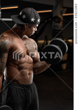 Strong and muscular dark skin man trains on modern equipment in gym. Portrait of muscular pumped up fitness trainer 83821063