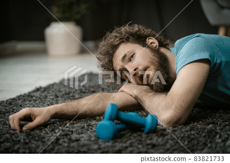 Exhausted Man After a Hard Workout Lies Tired on the Floor Next to Dumbbells. Lazy Guy Doesn't Want to Do Sports, Lack of Energy. Close-up 83821733