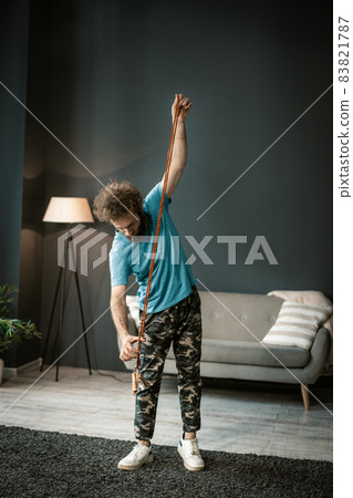Active Man Takes His Rope to Jump on It. Fit guy wants to start his morning fitness in his living room. Full-length 83821787