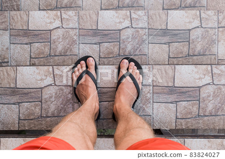 Men's legs in black flip flops and red shorts go down and walk down the stairs. Walking style 83824027