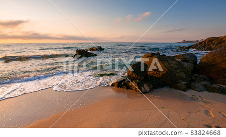 huge stones on the sandy beach at sunrise. wonderful velvet season vacation on the black sea in morning light. calm waves washing the shore of bulgaria. glowing clouds on the blue sky above horizon huge stones on the sandy beach at sunrise. wonderful velvet season vacation on the black sea in morning light. calm waves washing the shore of bulgaria. glowing clouds on the blue sky above horizon 83824668
